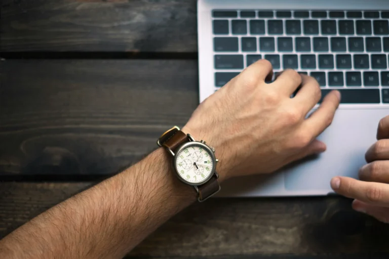 A man working on his laptop while checking his watch